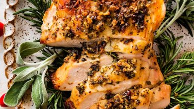 An air fryer turkey breast sliced sitting on a bed of fresh herbs and cranberries on a white platter.