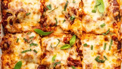 Healthy lasagna in a baking dish, cut into squares, and garnished with fresh basil and parsley.