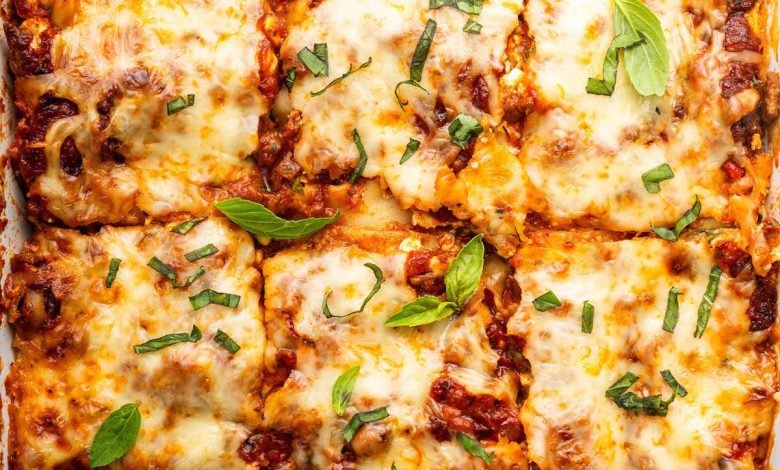 Healthy lasagna in a baking dish, cut into squares, and garnished with fresh basil and parsley.