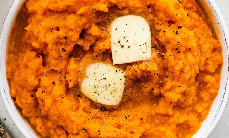 Mashed sweet potato in a bowl topped with two slices of butter and seasonings.