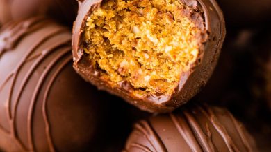 Chocolate covered peanut butter balls in a bowl with one ball having a bite taken from it.