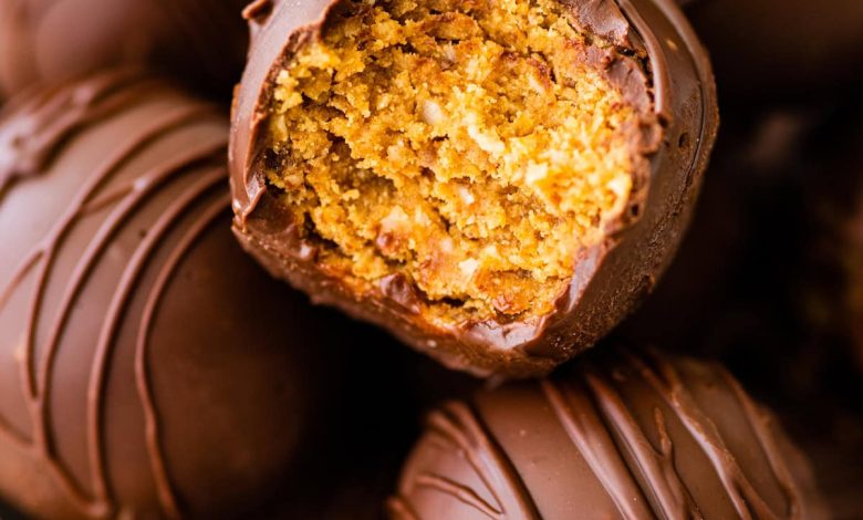 Chocolate covered peanut butter balls in a bowl with one ball having a bite taken from it.