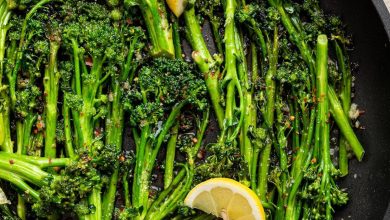 A pan of sautéed broccolini with lemon wedges and red pepper flakes.