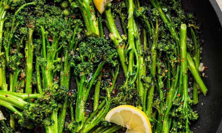 A pan of sautéed broccolini with lemon wedges and red pepper flakes.