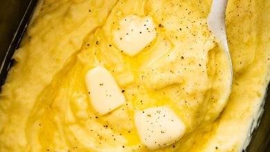 Mashed potatoes in a slow cooker with slices of butter, seasonings, and a spatula.