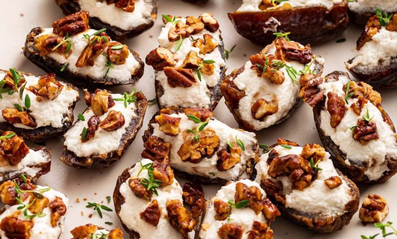 A large plate of multiple dates that are stuffed with goat cheese and topped with chopped pecans and fresh thyme.