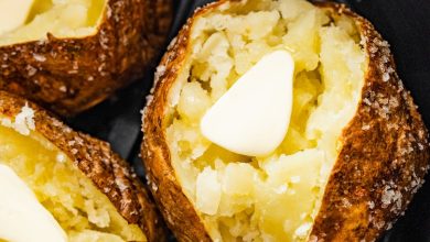 Three air fryer baked potatoes sliced open with butter in an air fryer.