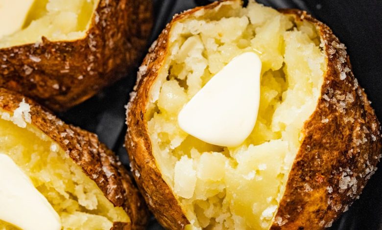 Three air fryer baked potatoes sliced open with butter in an air fryer.