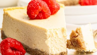 A slice of healthy cheesecake served on a white plate topped with fresh raspberries. A bite has been taken out of the slice.