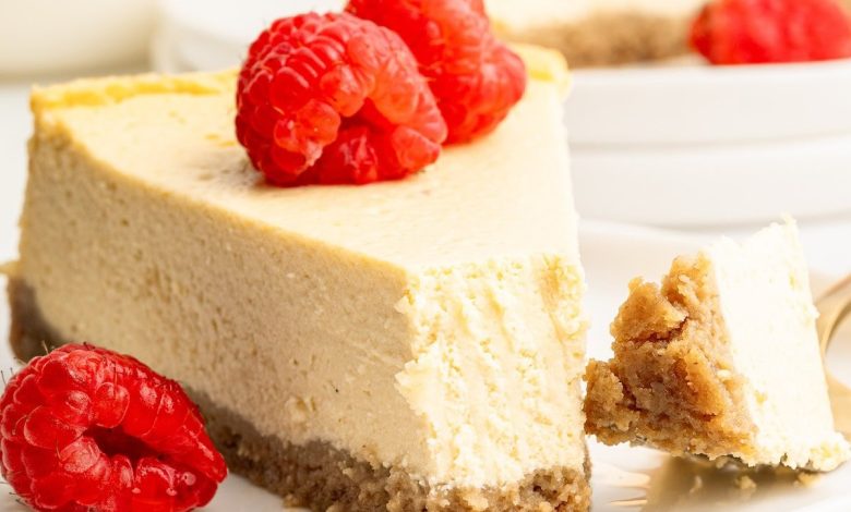 A slice of healthy cheesecake served on a white plate topped with fresh raspberries. A bite has been taken out of the slice.