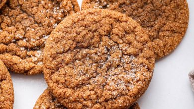 Multiple molasses cookies sprinkled with cane sugar with a glass of milk in the background.