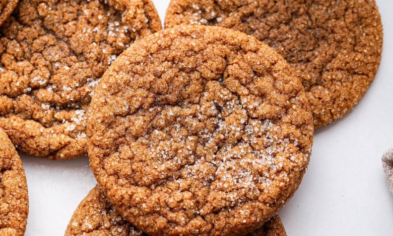 Multiple molasses cookies sprinkled with cane sugar with a glass of milk in the background.