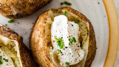 Three baked potatoes split open on a plate with sour cream, fresh chives, and seasoning.