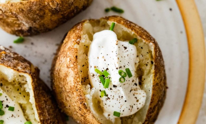 Three baked potatoes split open on a plate with sour cream, fresh chives, and seasoning.