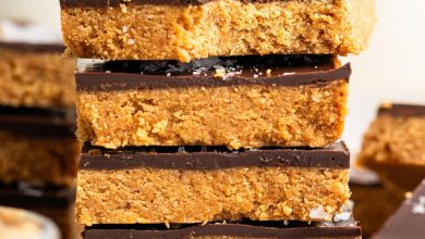 Four peanut butter bars stacked on top of each other on a wire cooling rack. The top bar has a bite taken out of it.