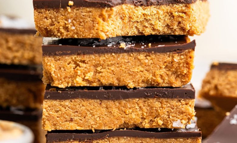 Four peanut butter bars stacked on top of each other on a wire cooling rack. The top bar has a bite taken out of it.