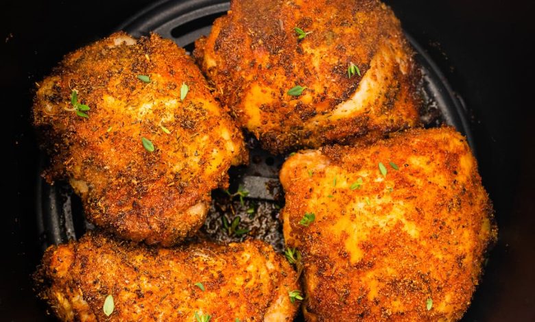 Four bone-in chicken thighs cooked in the basket of an air fryer topped with fresh parsley.