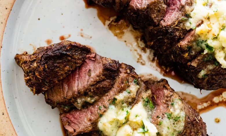 Two filet mignon pieces sliced on a white plate topped with garlic butter.