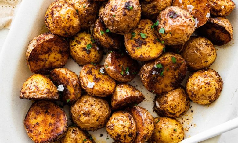 Crispy air fryer potatoes on a white plate garnished with fresh herbs and flaky sea salt.