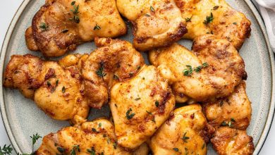 Baked boneless chicken thighs on a plate, garnished with fresh herbs.