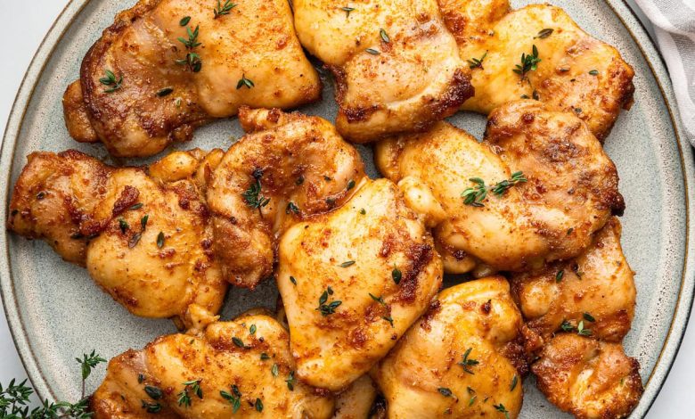 Baked boneless chicken thighs on a plate, garnished with fresh herbs.