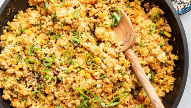 Cauliflower fried rice with eggs in a skillet with a wooden serving spoon. The dish is garnished with fresh green onion.