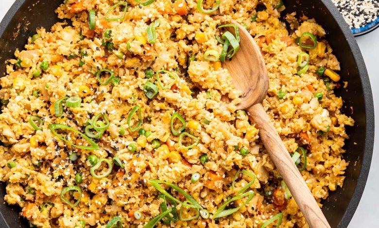 Cauliflower fried rice with eggs in a skillet with a wooden serving spoon. The dish is garnished with fresh green onion.