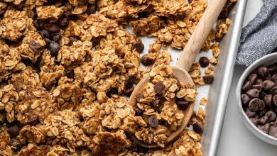 Clusters of chocolate chip cookie granola on a silver baking sheet served with a wooden spoon.