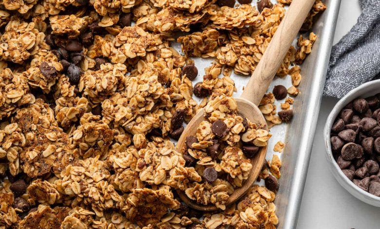 Clusters of chocolate chip cookie granola on a silver baking sheet served with a wooden spoon.