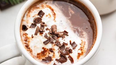 Two white mugs of hot chocolate topped with a little whip cream and chocolate shavings.