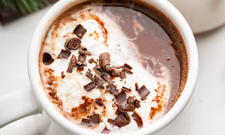 Two white mugs of hot chocolate topped with a little whip cream and chocolate shavings.