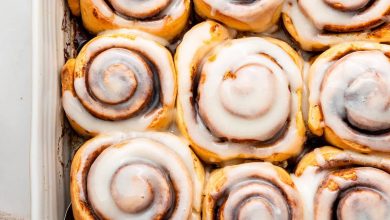 A white square baking dish filled with 9 baked cinnamon rolls that are topped with a glaze.