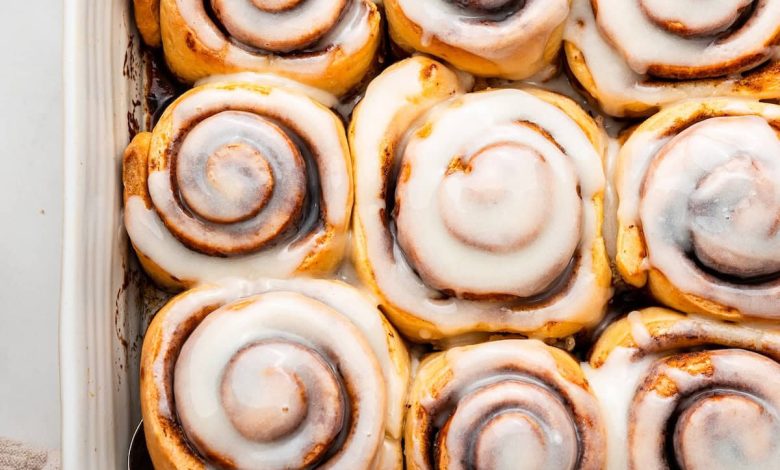 A white square baking dish filled with 9 baked cinnamon rolls that are topped with a glaze.