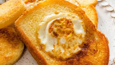 A slice of toast on a plate with the center cut out of it. A cooked egg is in the center of the slice of bread.