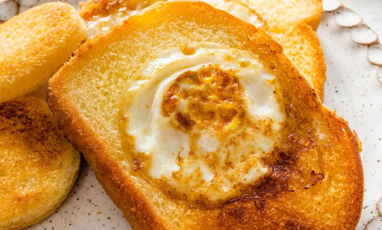 A slice of toast on a plate with the center cut out of it. A cooked egg is in the center of the slice of bread.