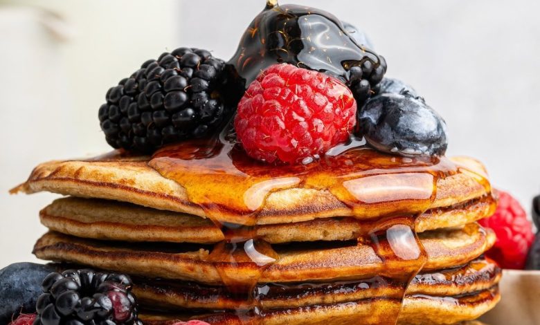 Maple syrup being poured on top of a stack of six greek yogurt pancakes on a plate. They