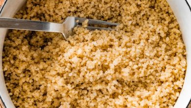 A large white pot filled with cooked quinoa. There is a silver fork in the quinoa.