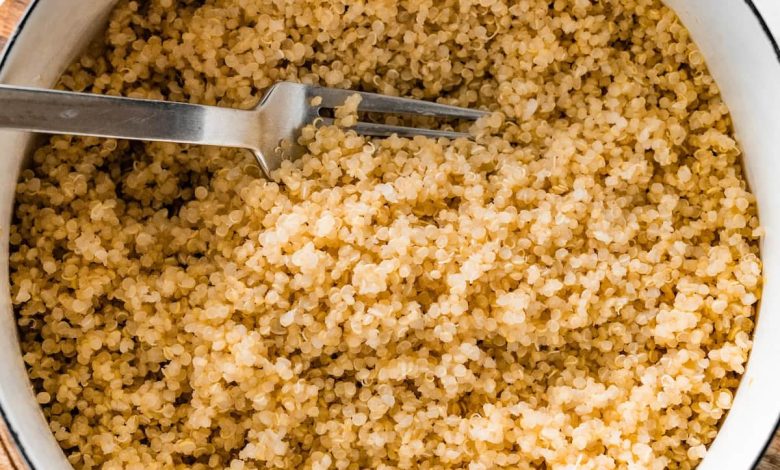 A large white pot filled with cooked quinoa. There is a silver fork in the quinoa.