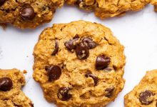 Multiple peanut butter oatmeal cookies with chocolate chips spread out on a table. One of the cookies has a bite taken out of it.