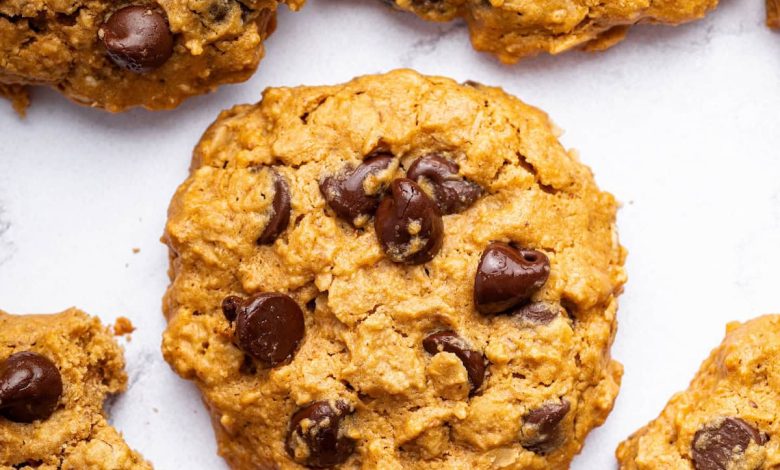 Multiple peanut butter oatmeal cookies with chocolate chips spread out on a table. One of the cookies has a bite taken out of it.