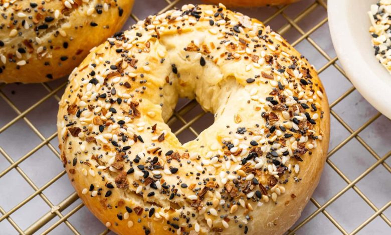 Four everything bagels on a gold cooling rack.