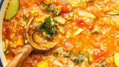 A large pot of vegetable packed quinoa soup with a wooden serving spoon in the soup.