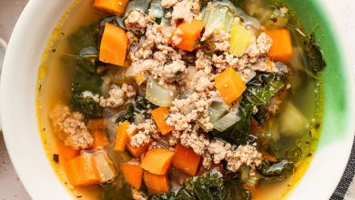 Sausage and kale soup served up in a green and white soup bowl.