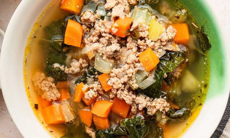 Sausage and kale soup served up in a green and white soup bowl.