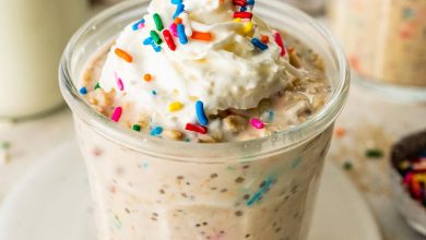 A glass jar filled with birthday cake overnight oats, topped with whipped cream and colorful sprinkles, with a bottle of milk and another jar of oats in the background.