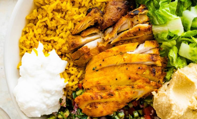 A chicken shawarma bowl with turmeric rice, sliced chicken shawarma, romaine lettuce, Shirazi salad, hummus and Toum.