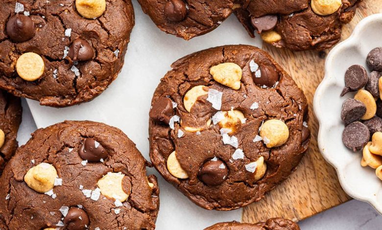 9 chocolate peanut butter cookies spread out on a counter. All of the cookies are topped with flaky sea salt.