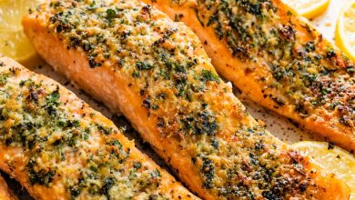 Four parmesan crusted salmon filets served on a speckled tray with multiple lemon slices.