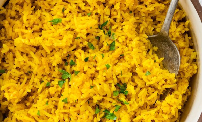 A pot of cooked turmeric rice topped with fresh parsley. There is a silver spoon in the rice.