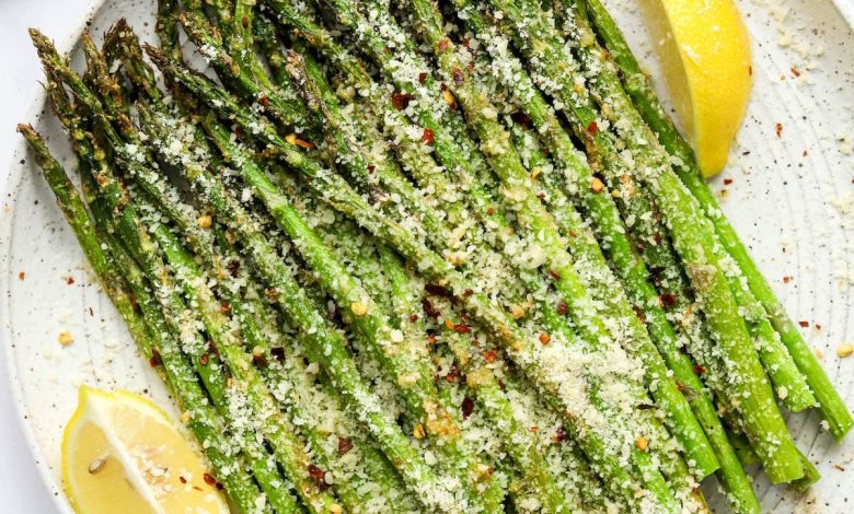 A plate with asparagus and lemon wedges topped with cheese and red pepper flakes.